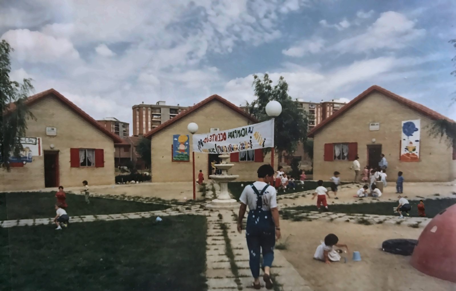 Foto histórica de 1989 de la Escuela Infantil El Huerto, con niños jugando en la plaza junto a la fuente.