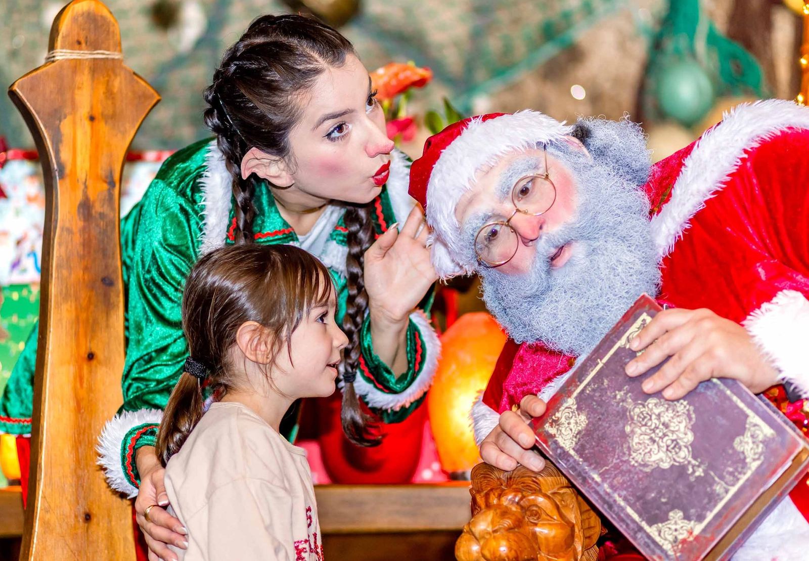 Papá Noel y una de sus elfas enseñan el libro mágico a una niña en la casa de Papá Noel de La Granja de los Cuentos.