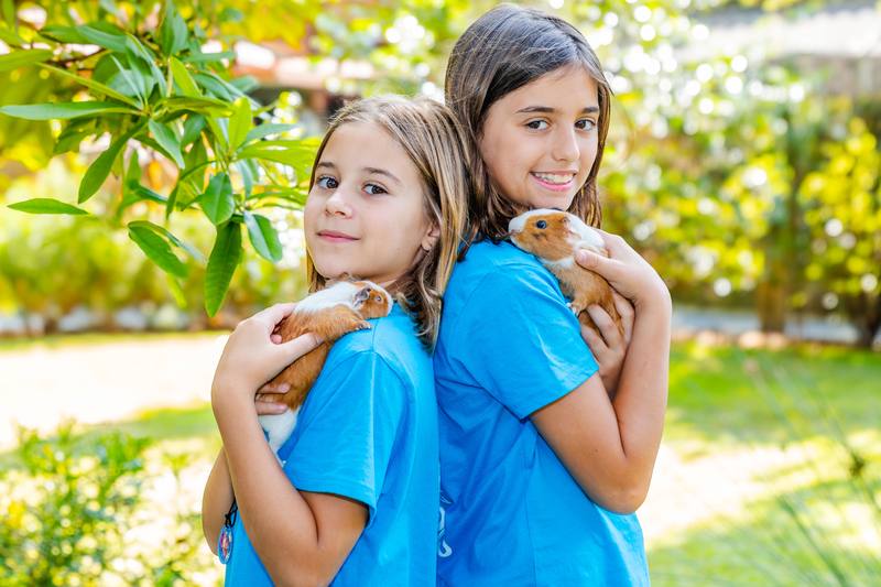 Dos niñas sostienen cada una una cobaya en brazos, sonriendo.