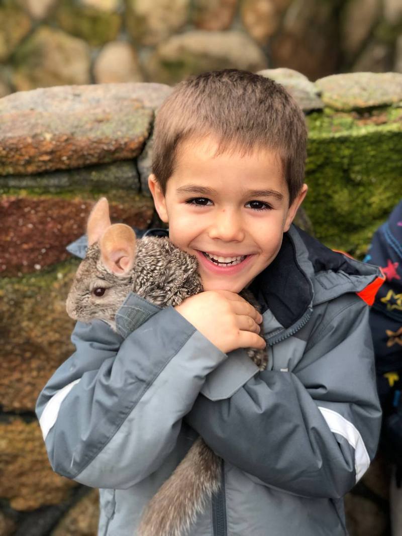 Un niño sonríe sujetando con las dos manos un animal pequeño contra su pecho.