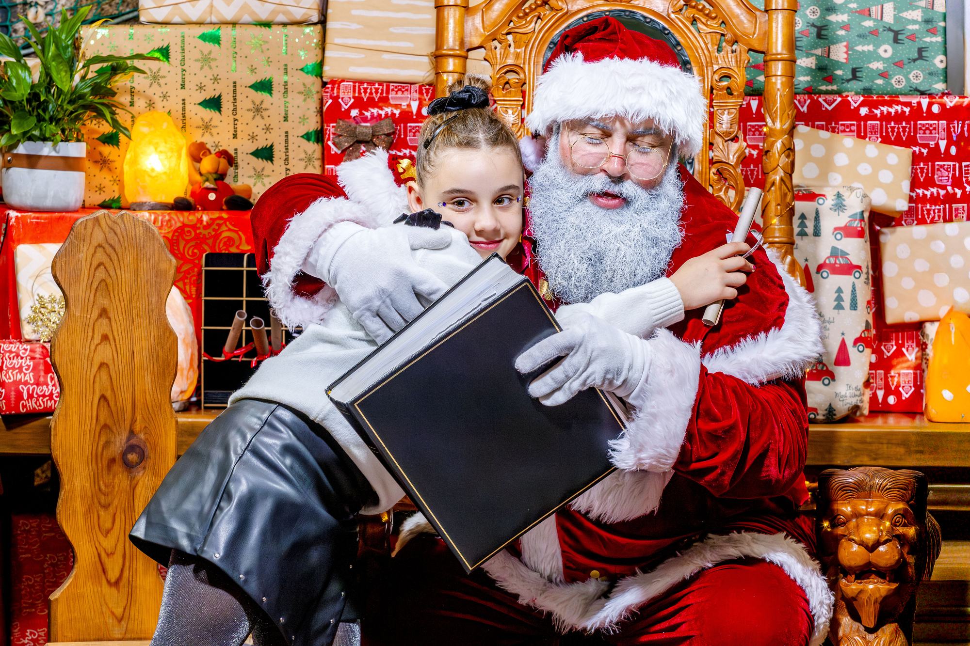 Papá Noel abrazado a una niña mientras consulta el libro mágico con sus secretos, en La Granja de los Cuentos.