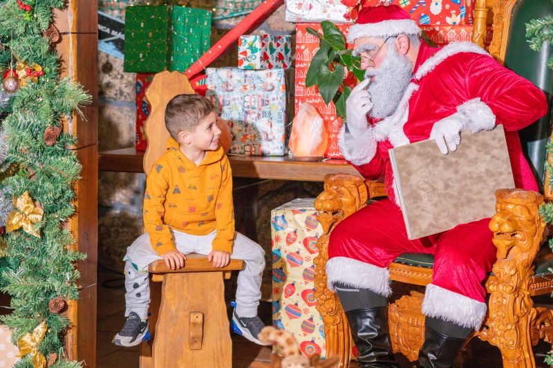 Un niño sonríe mirando a Papá Noel, sentado en su sillón con un libro, en La Granja de los Cuentos.