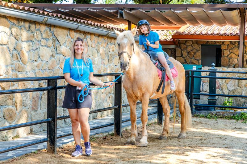 Una niña monta a caballo en el picadero acompañada por una monitora que lleva las riendas.
