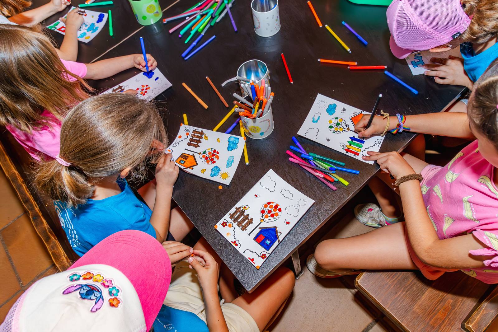 Manos de niños pintando sobre una mesa llena de rotuladores de colores en el taller.